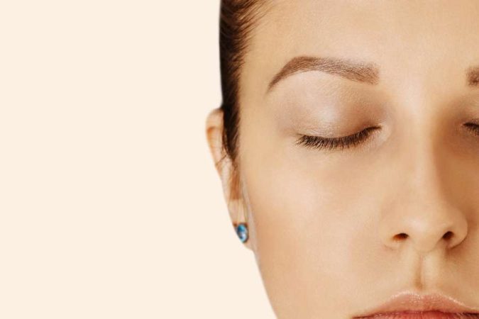 Gros plan d'une femme aux yeux fermés, sourcils soignés et peau nette, illustrant comment sublimer son regard sans maquillage.