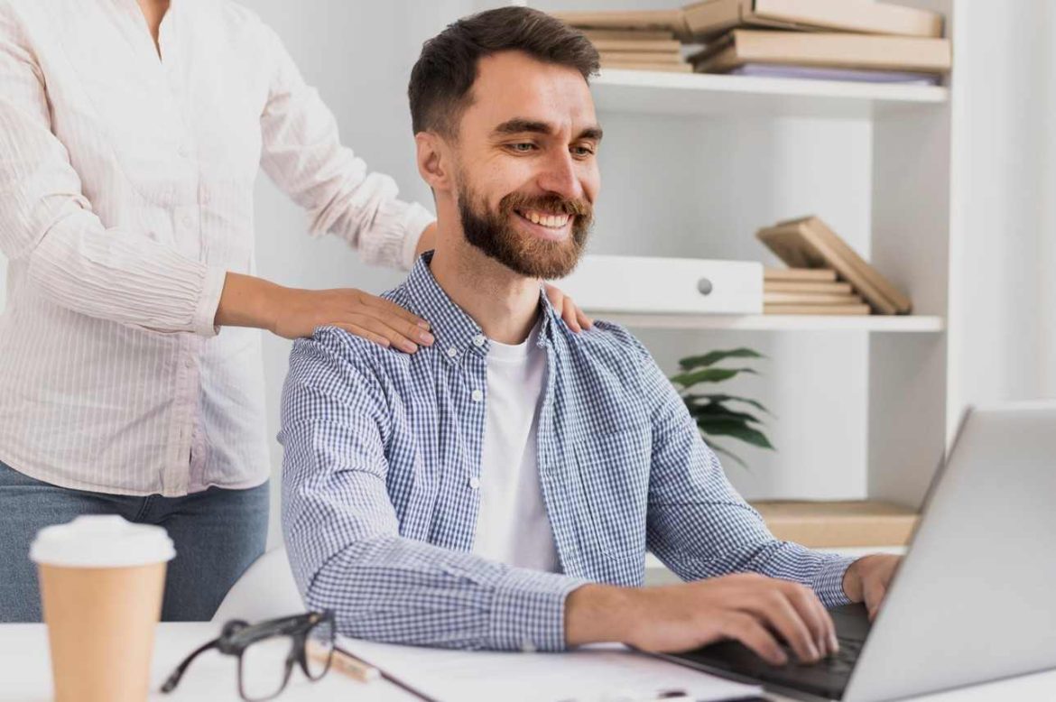 Un employé souriant recevant un massage en entreprise bien être au travail tout en travaillant sur son ordinateur portable.