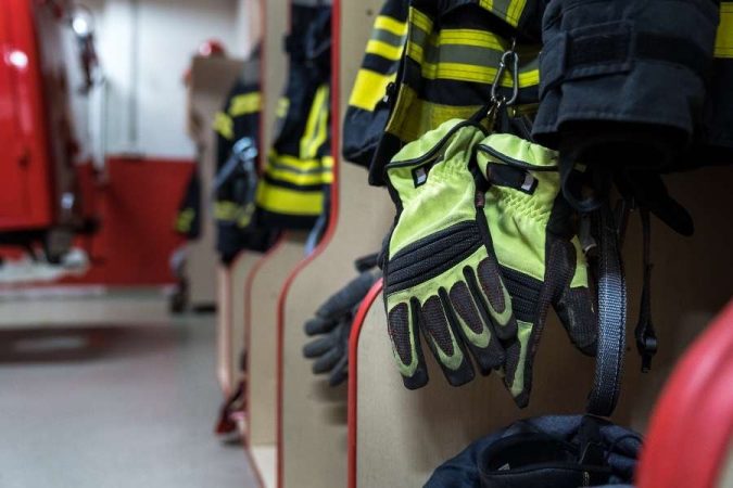 Une paire de gants de protection jaune fluo et noir accrochée dans le vestiaire d'une caserne de pompiers.