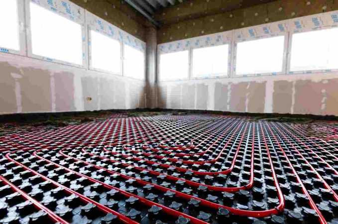 Pose de tuyaux de plancher chauffant sur des dalles isolantes dans une grande pièce lumineuse en construction